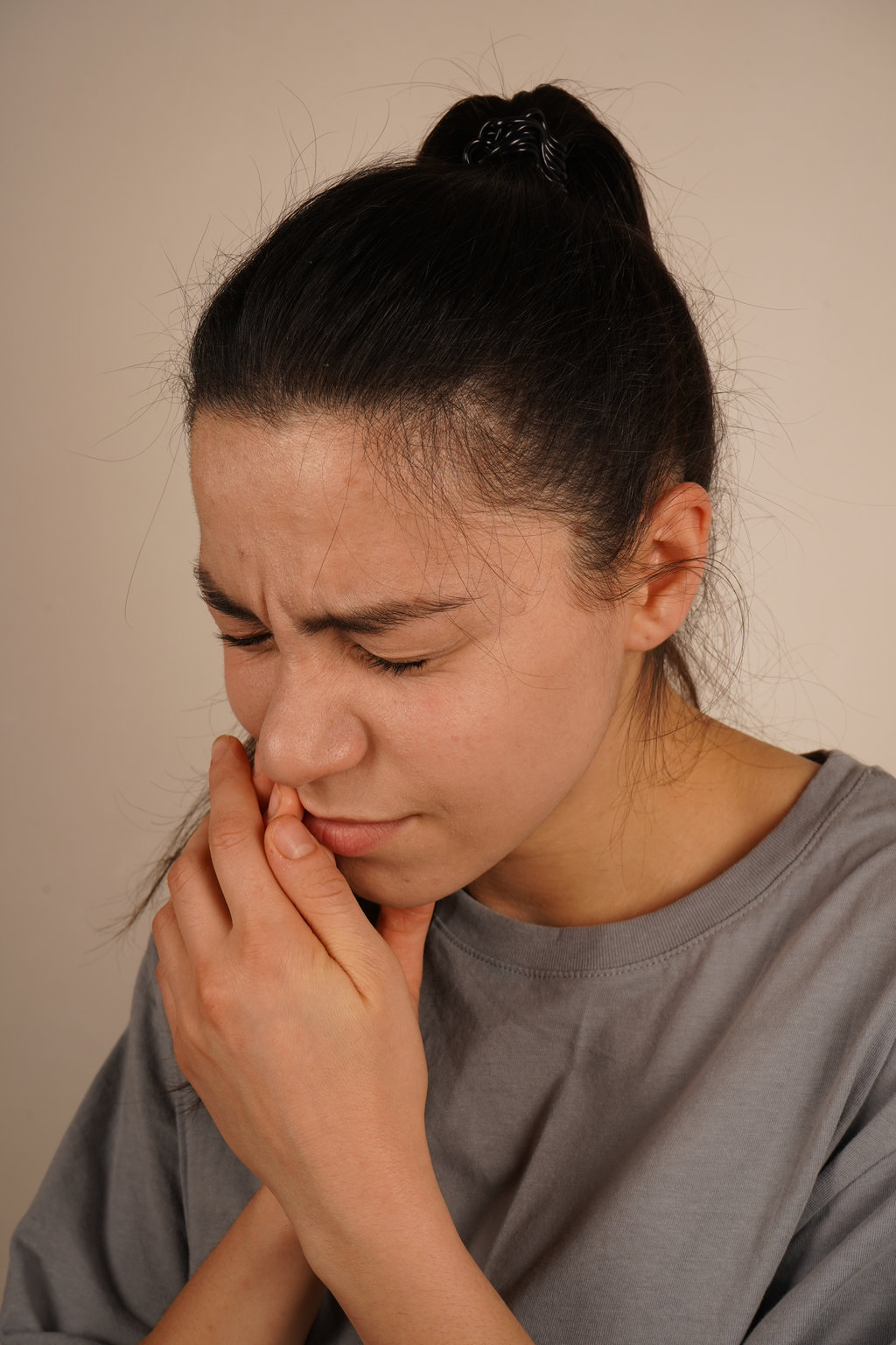 The woman clutches her gum with a pained expression, capturing the sensation of a toothache. Her body language reflects physical discomfort. The moment is a genuine depiction of personal unease