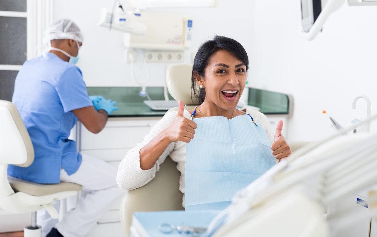 Whitehall, PA 2 Happy latin american woman sitting in dental chair after teeth cure in modern clinic, gesturing thumbs up